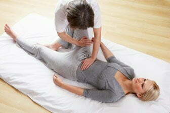 Woman applying acupressure to another woman lying on a mat on the floor